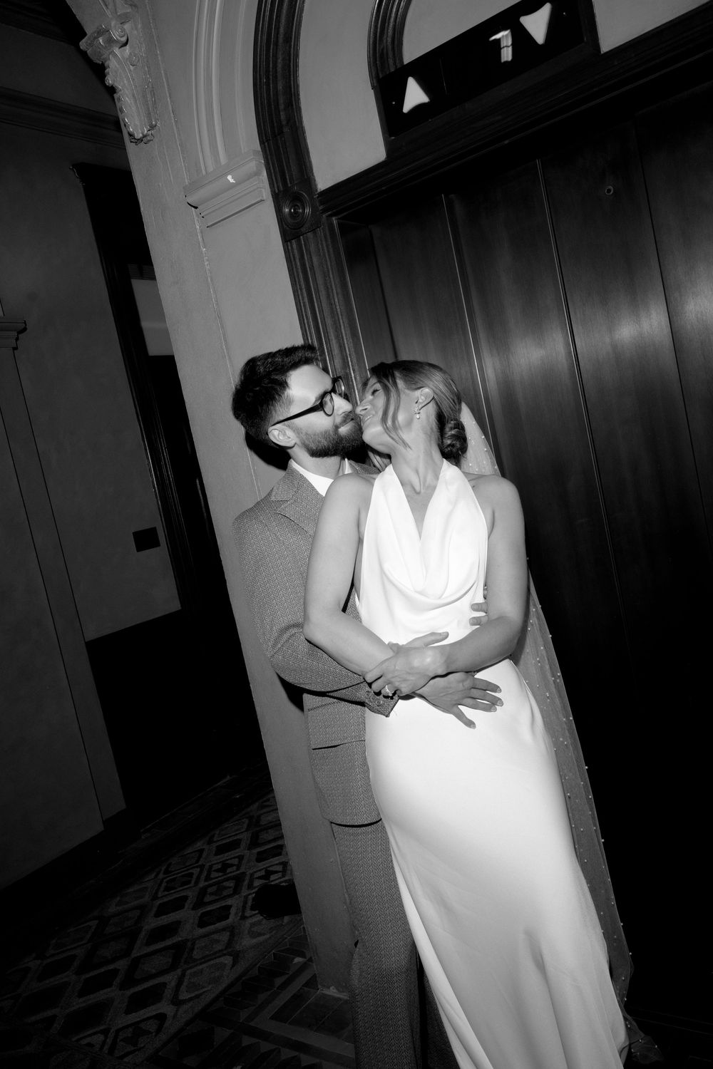 Black and white photo of bride and groom sharing a kiss by an elevator in a historic building.