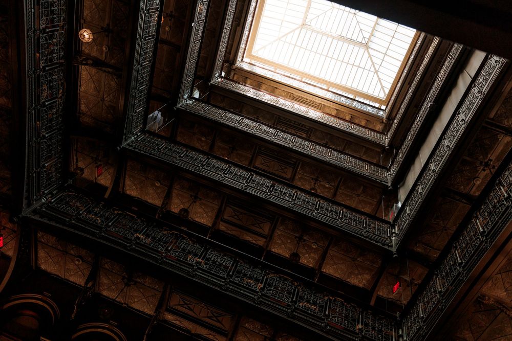 Looking up through dramatic square skylight framed by intricate dark carved wooden architectural details.
