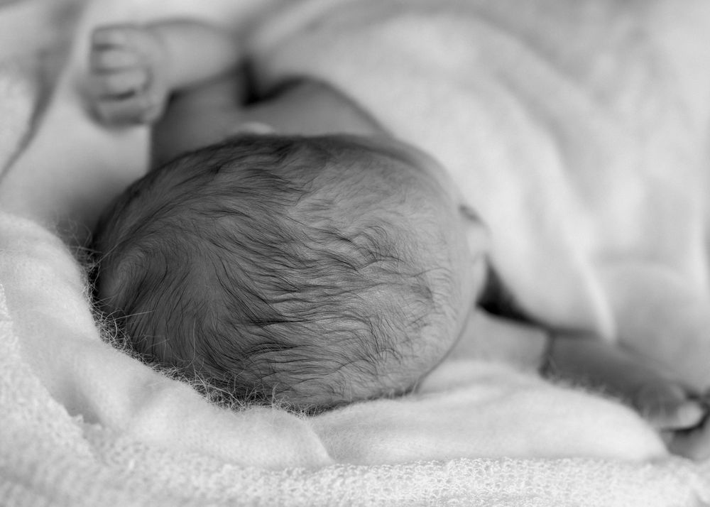 Black and white image of newborn head and close up of wavy black hair. Neutral colours, textured knits. Newborn family photographer auckland