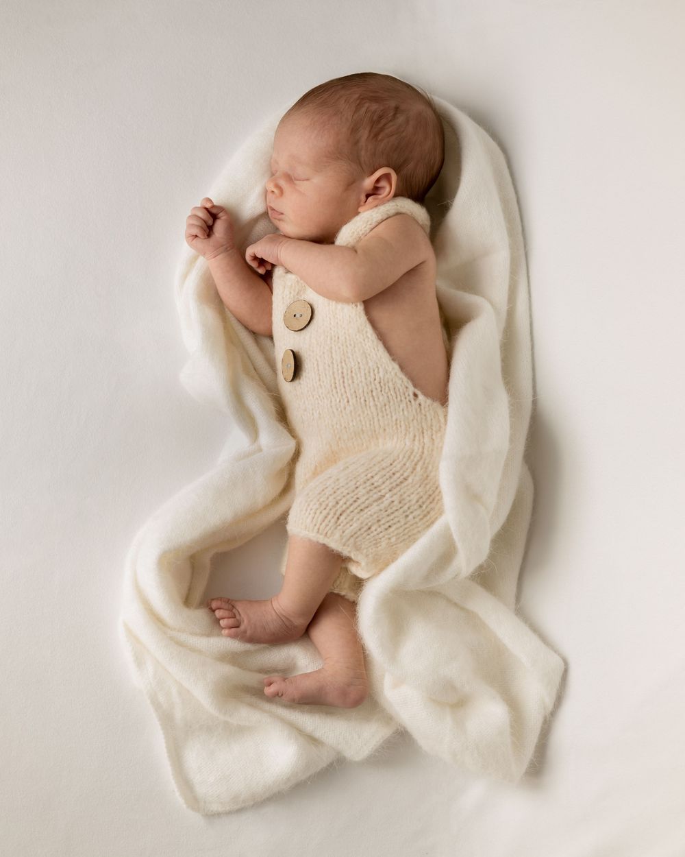 Newborn baby sleeping on side for a lifestyle Newborn photoshoot, wearing white knits, textures. Auckland newborn photographer