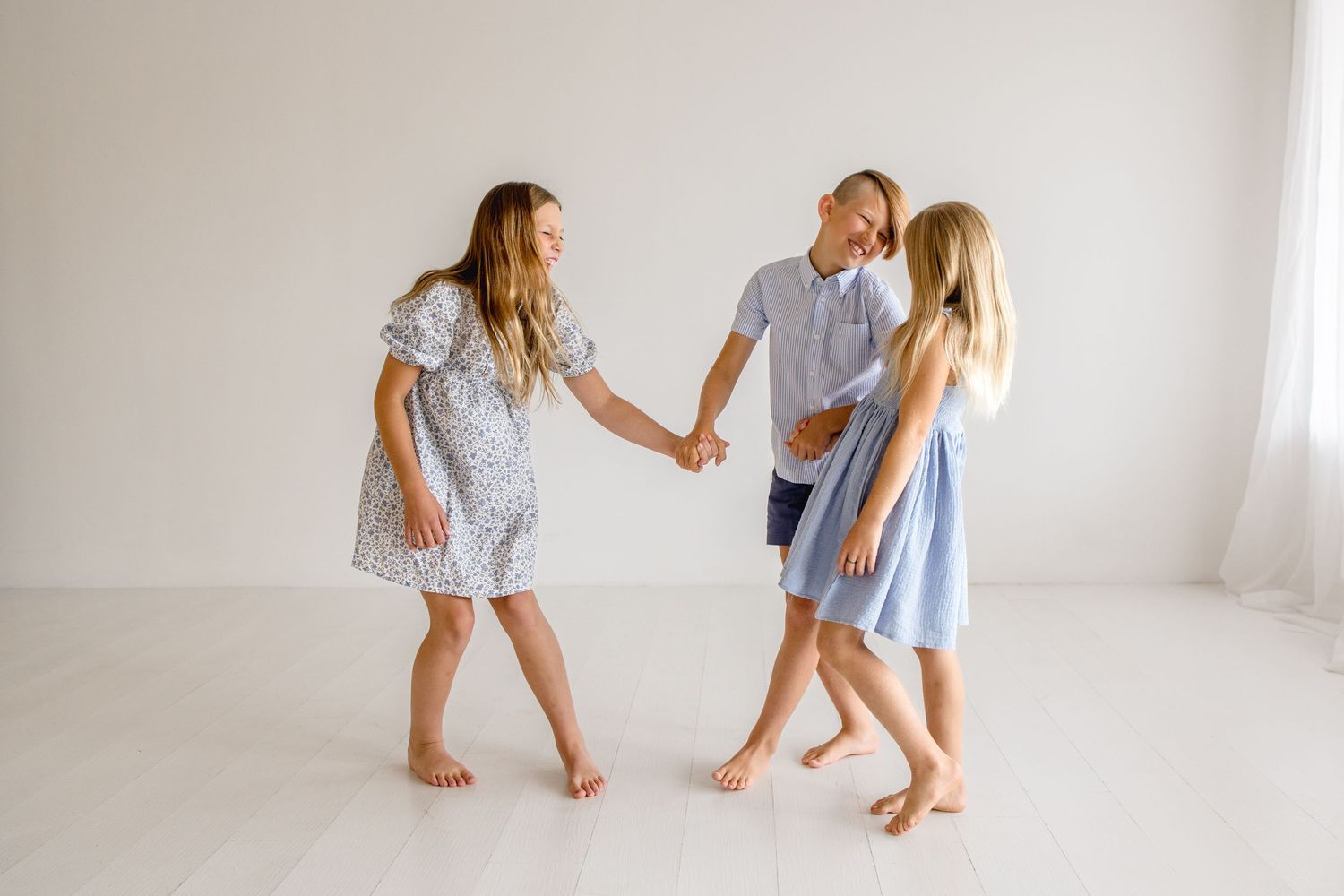 Two children in light blue and white outfits playing together against a bright white backdrop.