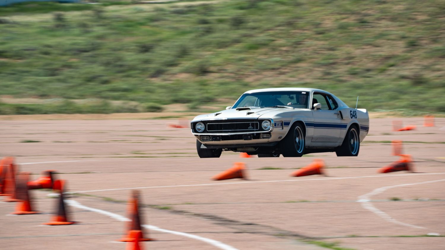 Classic silver Ford Mustang navigating through orange cones on an autocross course during a racing competition.