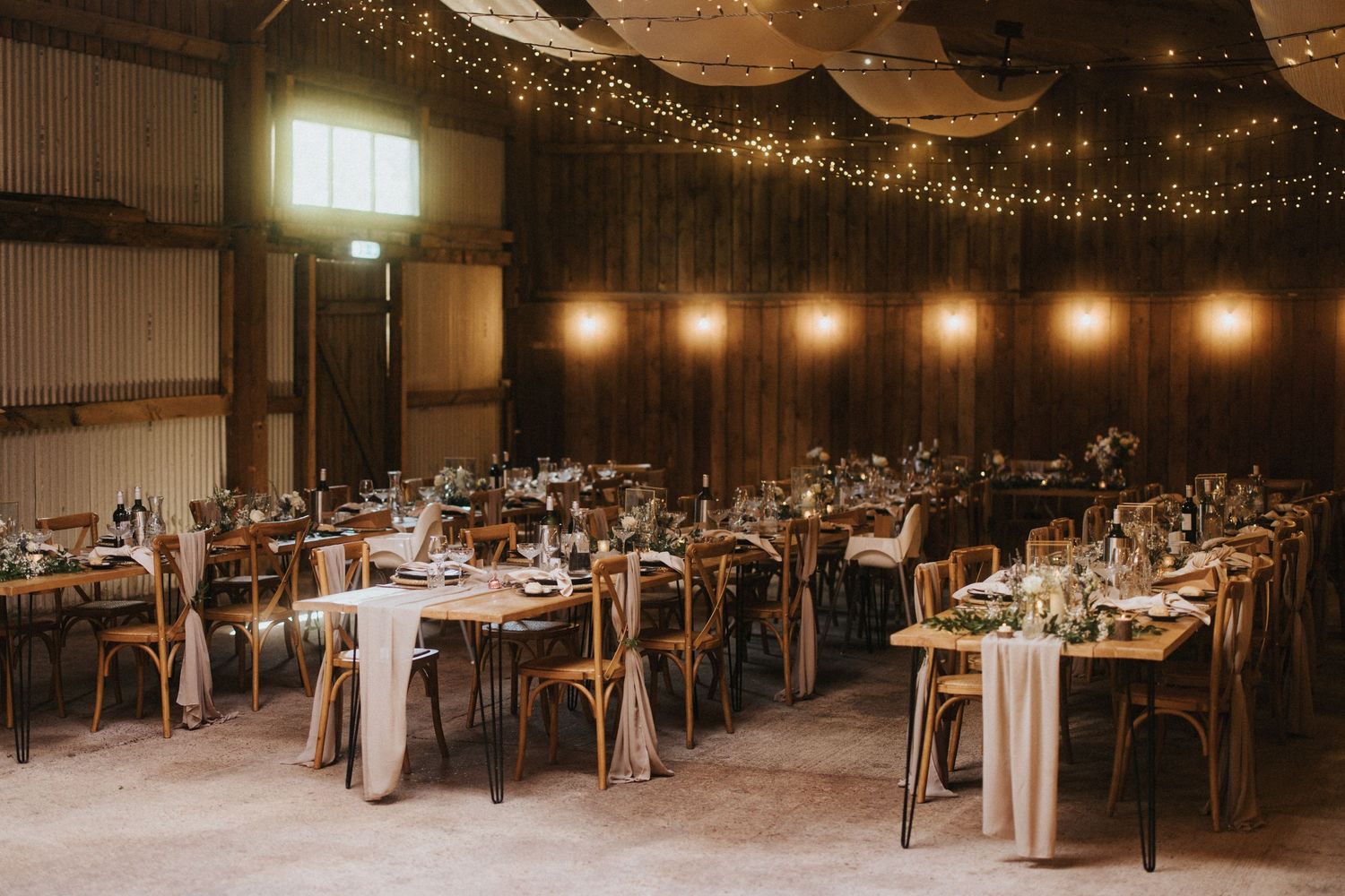 Reception tables set up in a rustic barn venue with romantic string lights and wooden beams creating an elegant atmosphere.