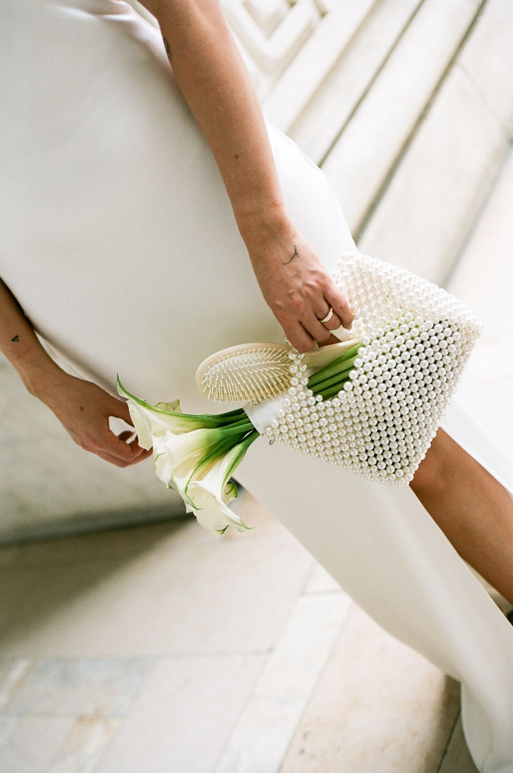Hands holding a delicate white mesh bag with elegant calla lilies against a light background.