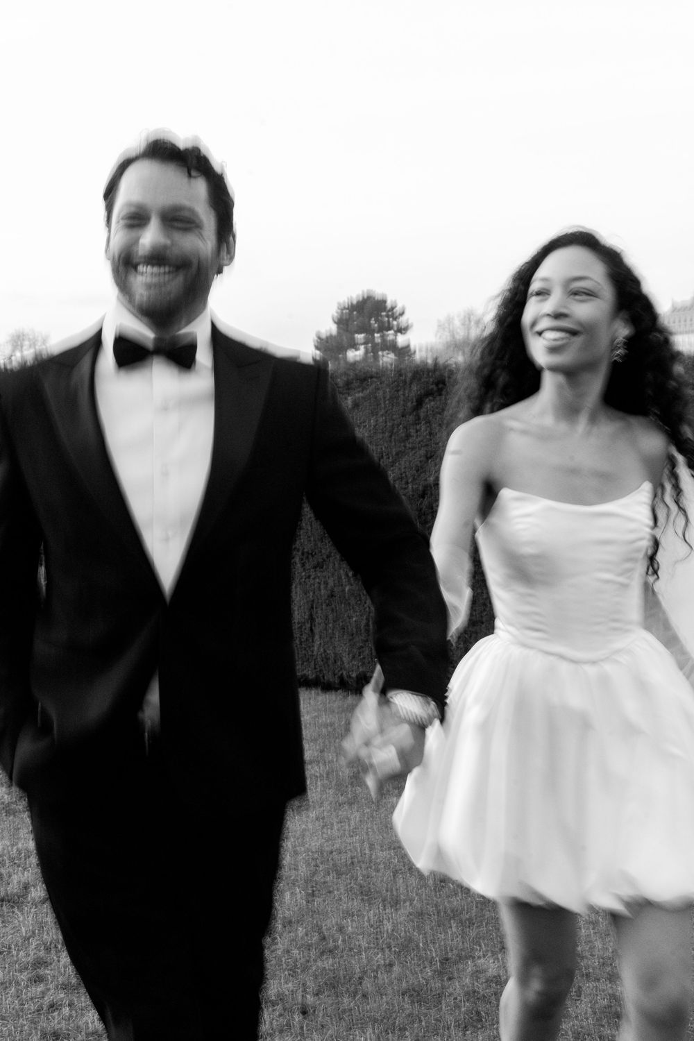 A joyful wedding couple in formal attire dances and laughs together outdoors in black and white photographs.