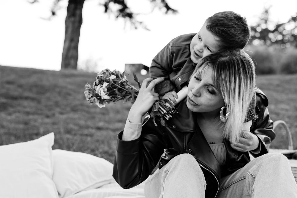 Black and white photo of a couple sharing a tender moment outdoors, woman holding a bouquet of flowers.