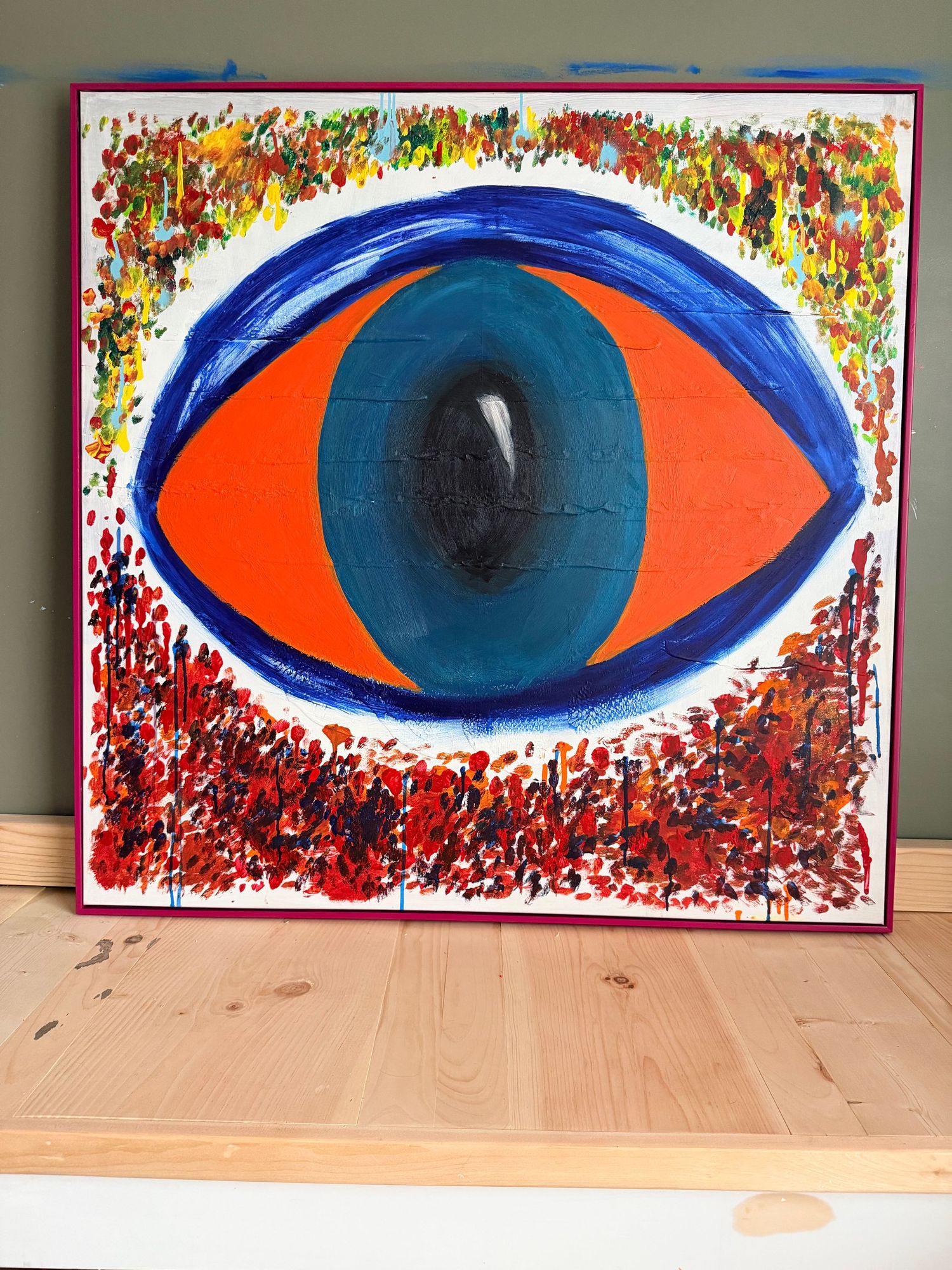 Vibrant psychedelic eye painting on black canvas with yellow, blue, and red abstract patterns in a wooden frame.