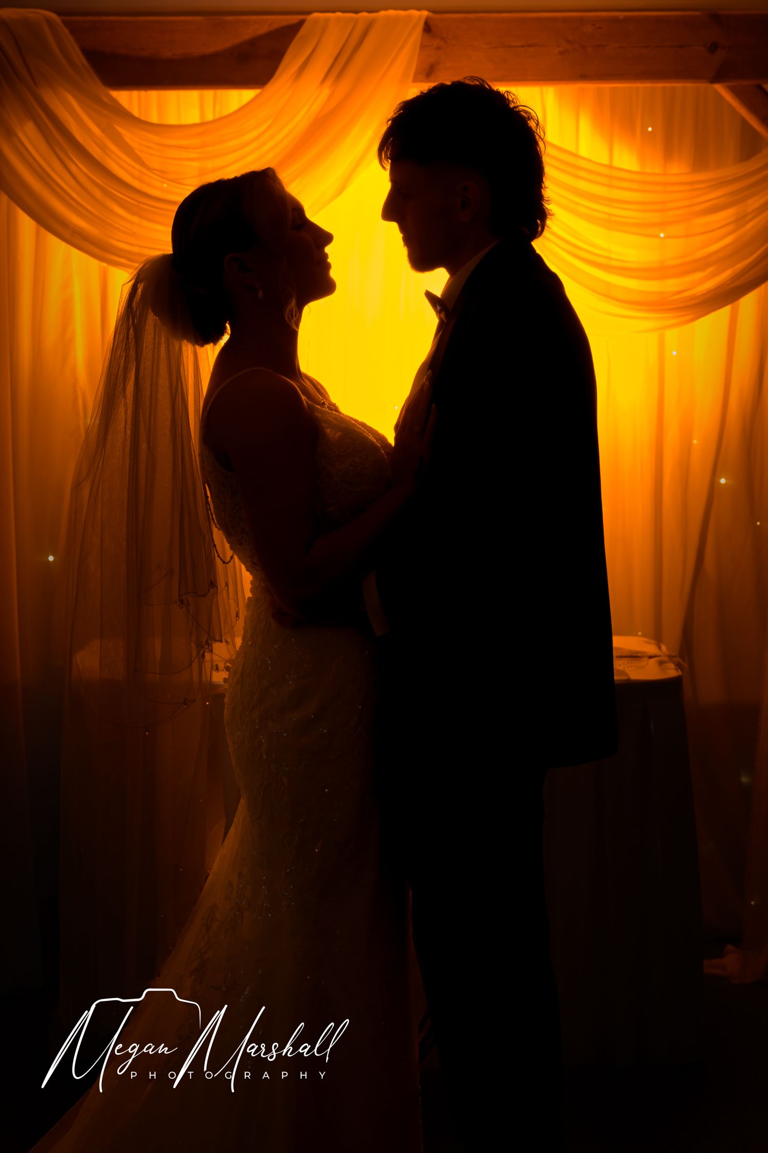 Silhouette of bride and groom facing each other in romantic golden backlit wedding portrait.