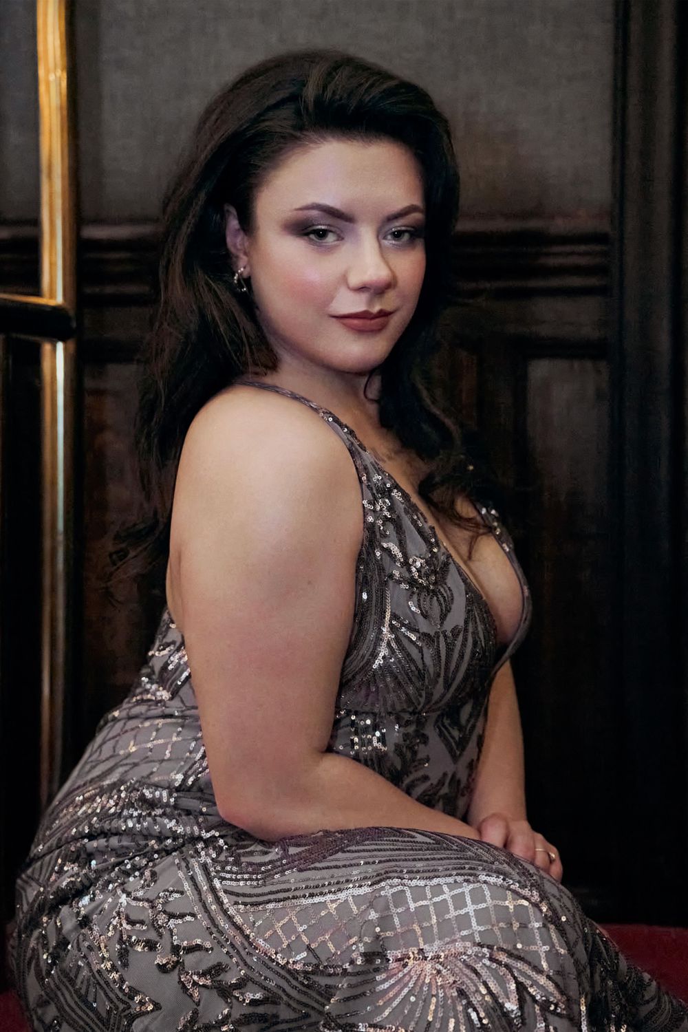 Elegant woman in silver sequined dress with deep V-neckline poses in luxury hotel.