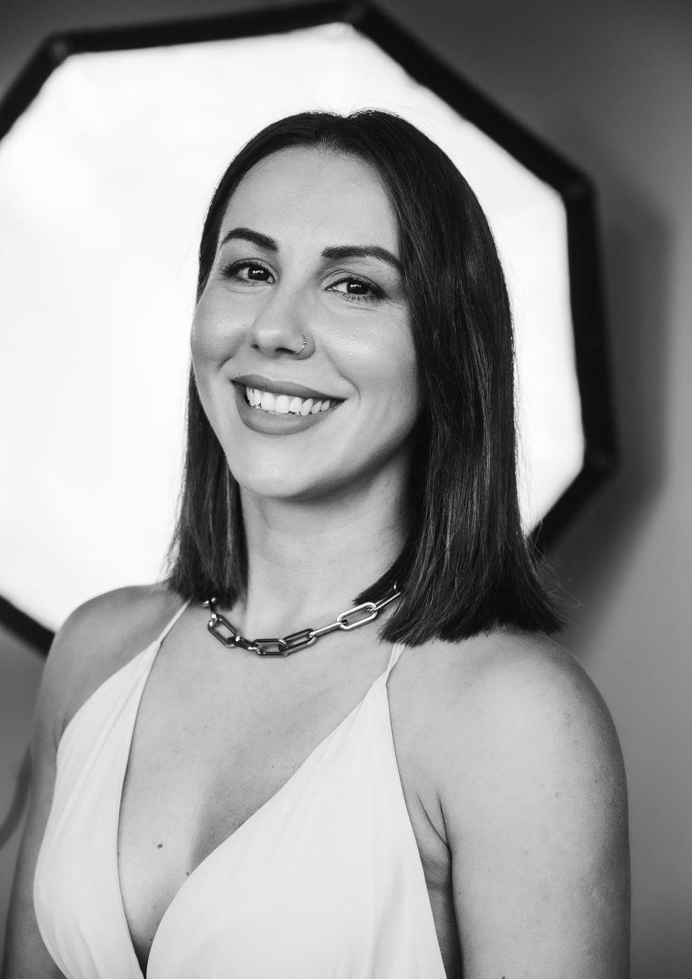 Black and white portrait of smiling brunette woman wearing chain necklace and white top.