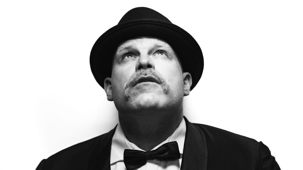 Black and white low angle portrait of man in fedora and bow tie looking upward.