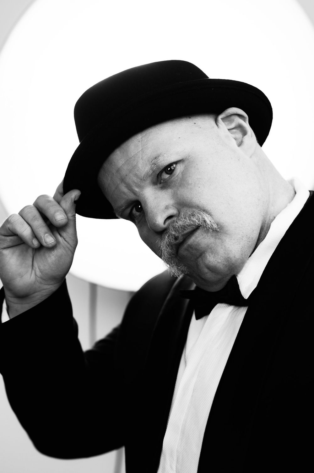 Black and white portrait of man in tuxedo tipping his bowler hat with a serious expression.