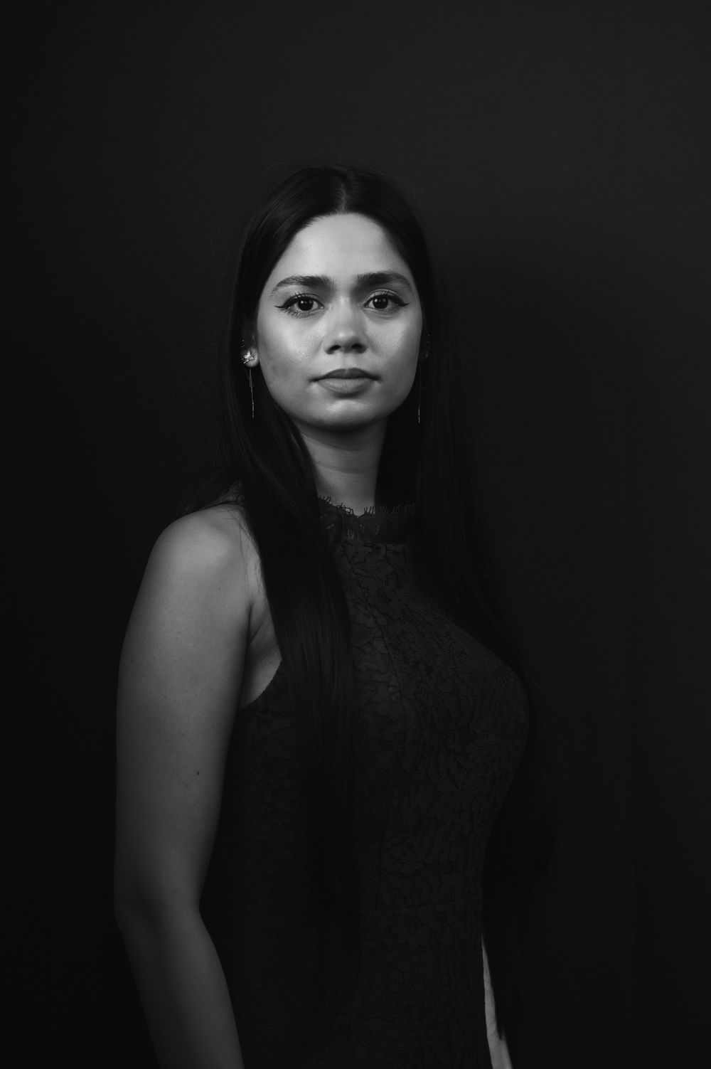 Black and white full-length studio portrait of a young woman in a sleeveless dress on dark background.