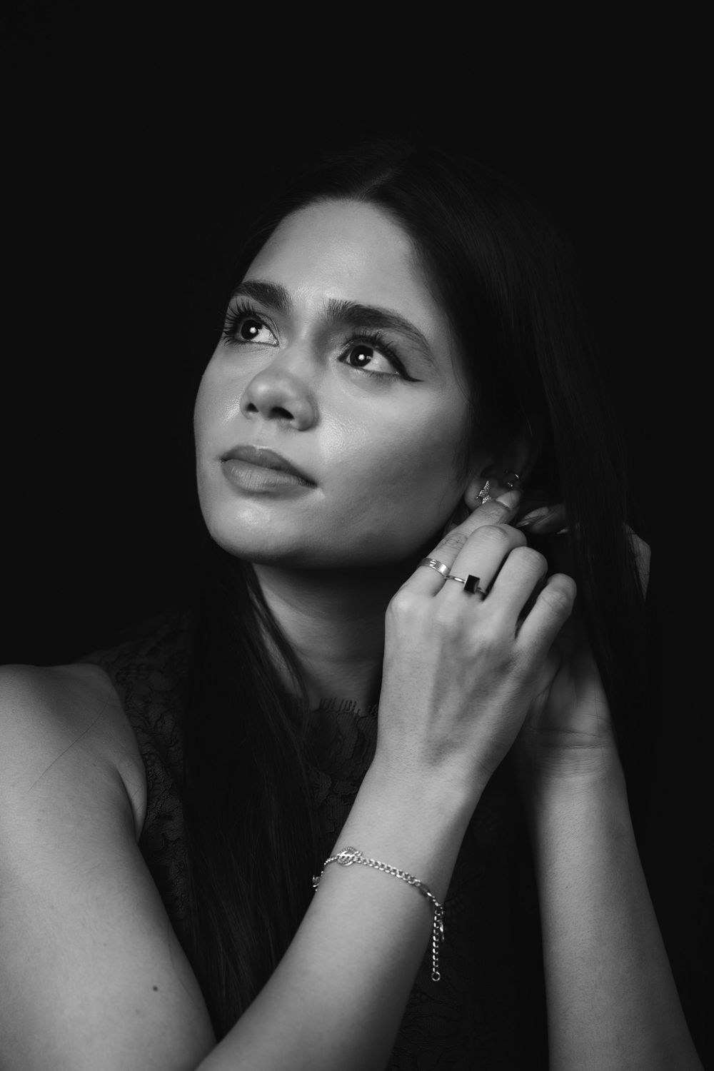 Black and white portrait of a young woman touching her hair wearing a bracelet and rings.