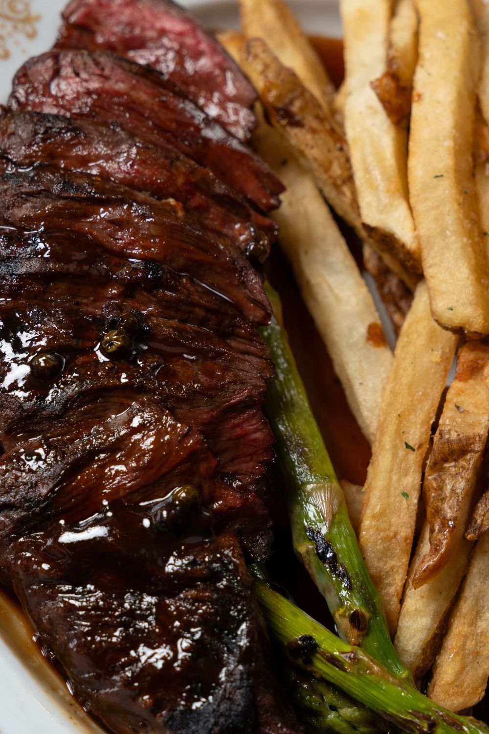 Grilled skirt steak with charred scallions and crispy french fries served on a white plate.