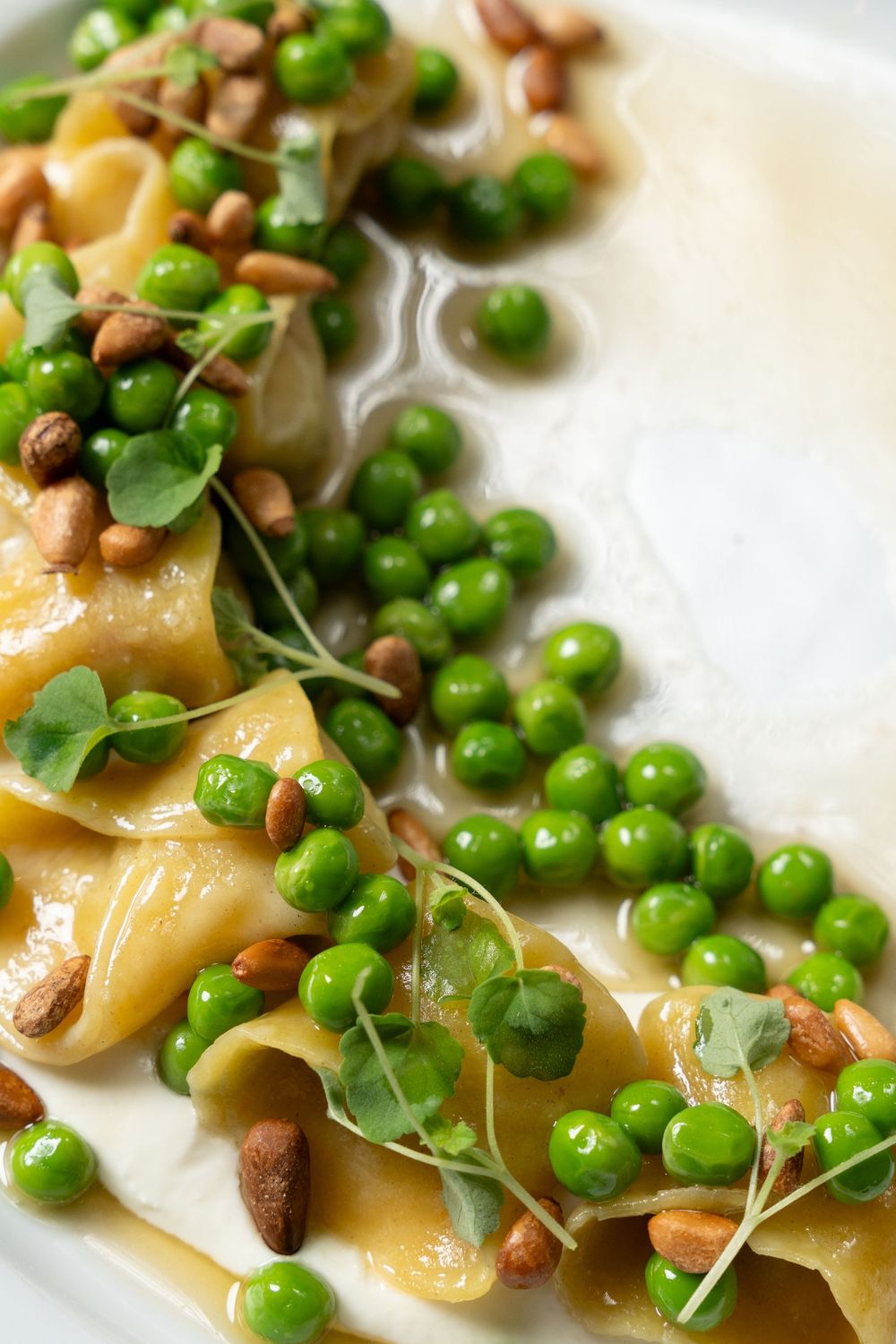 Elegant pasta dish with green peas, pine nuts, and microgreens in creamy sauce on white plate.
