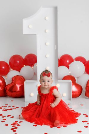Valentines themed baby photos in Menifee: Baby girl in red dress with red and white balloons for first birthday.
