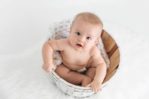 Cute baby sitting in a wicker basket on a white fluffy blanket during a professional photo session.