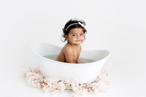 8 month old baby photoshoot in Menifee; smiling baby girl sitting in a white bathtub surrounded by pink flowers.