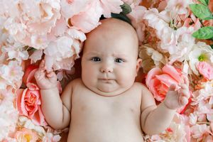 Professional Menifee photographer photo of adorable baby girl lying among pink and white floral arrangement looking at camera.