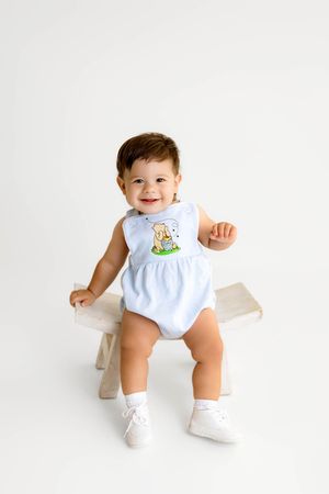 Smiling baby boy's 1st birthday photoshoot in Winnie the Pooh outfit.