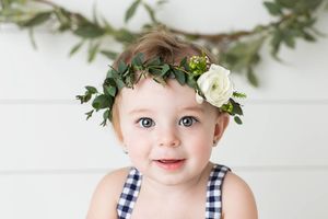 Beautiful baby girl smiling for professional portrait in a floral flower crown headpiece.