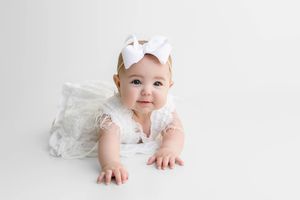 Adorable baby girl in white lace outfit smiling on a clean white background.