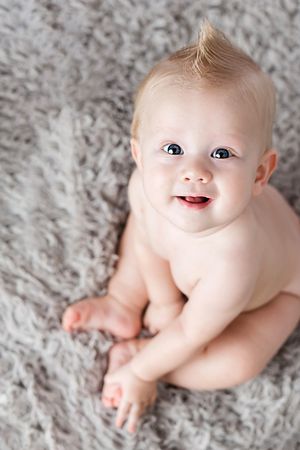 Happy smiling baby boy sitting on fluffy gray carpet.