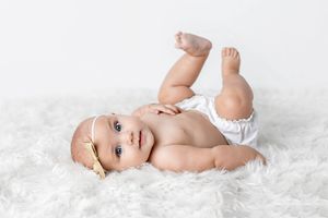 Professional 6 month photo of smiling baby girl in white diaper lying on fluffy white rug.