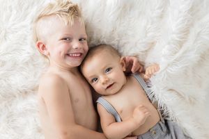 Menifee family and sibling photographer: Smiling toddler boy hugging his baby brother in a white fluffy rug in an adorable sibling portrait.