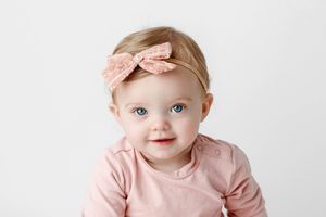 Temecula professional photographer's headshot of adorable baby girl with blue eyes wearing pink bow headband and pink outfit.
