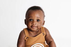 Adorable 6 month old baby boy in neutral rainbow romper on white background.