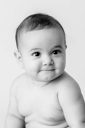 Black and white portrait of a chubby smiling baby with dark eyes on a light background by professional infant photographer.