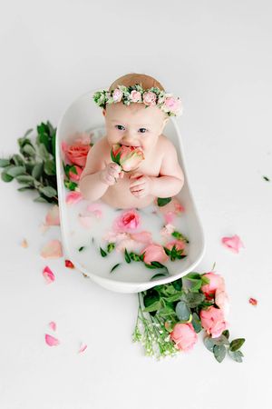 Baby girl sitting in a milk bath with pink roses wearing a floral crown, in Southern California professional photography studio.