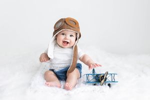 Happy baby wearing aviator hat sitting with toy airplane for 6 month photos.