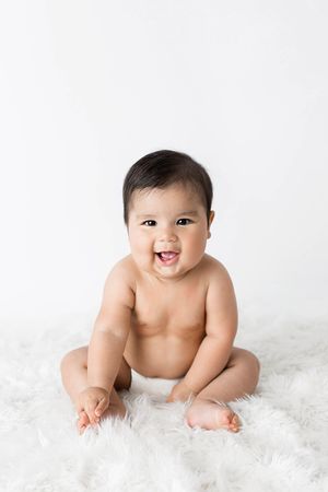 Happy baby sitting on white fluffy rug for 6 month photoshoot in Temecula.