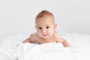 Sweet baby lying on white blanket for 6 month photos.