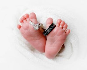 Professional newborn photography studio in Menifee: Tiny newborn baby feet with parents wedding rings posed on white knit blanket.