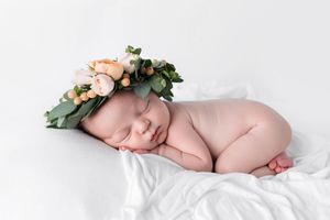 Sleeping newborn baby wearing floral crown with peach roses on white blanket.
