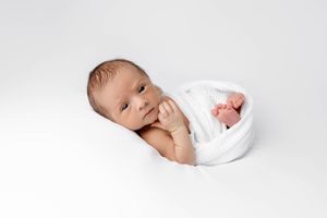 Alert newborn baby wrapped in white swaddle looking at camera.