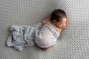 Sleeping newborn baby wrapped in gray blanket on textured gray knit surface.