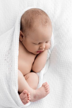 Peaceful newborn baby sleeping wrapped in a soft white knit blanket.