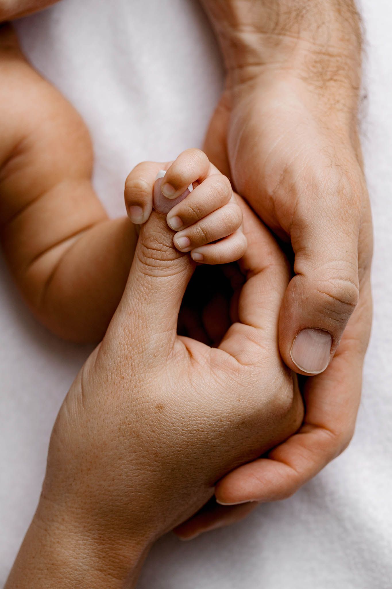 Close-up of a newborn baby's tiny hand gently gripping parents fingers.