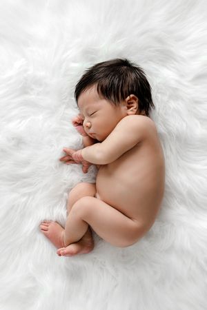 Minimalist newborn photographer: Sleeping baby boy lying on soft white fluffy blanket.