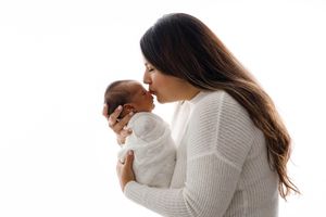 Temecula infant photographer: Mom kissing her swaddled newborn baby on white background.