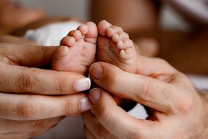Close-up of parents hands gently holding tiny newborn baby feet.