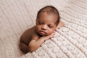 Newborn baby sleeping on cream knit blanket in classic posed newborn photography.