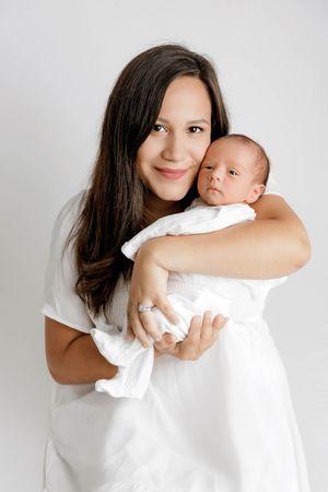 Timeless professional mom and baby photographer in Riverside area: Smiling mom in white dress holding her newborn baby boy.