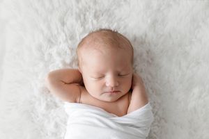 Sleeping newborn baby swaddled in white wrap.