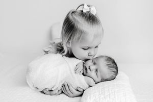 Family newborn sibling photographer: Black and white photo of toddler girl kissing sleeping newborn baby brother.
